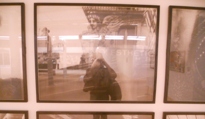 A sepia photograph of a person's reflection in framed photographs of buildings.