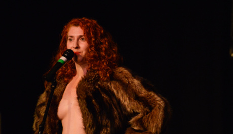 A long, wavy red-haired woman stands up to the mike,wearing an open fur coat and nothing else