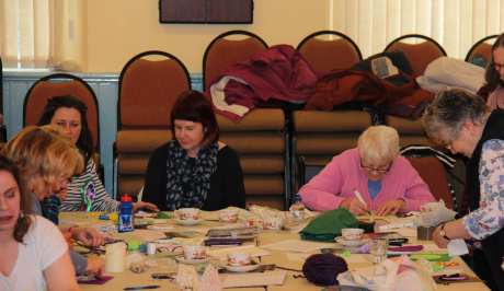 five women sit around a table full of bits of sewing materials, working on the banners for the processions. 