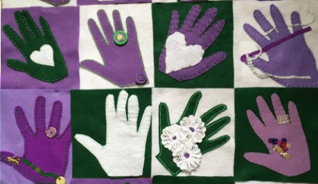 A piece of appliqued fabric, with cut out hands and symbols sewn on in the suffragette colours of white, purple and green.