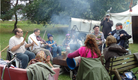 A group of diverse people sitting around a campfire, with smoke flowing, they are singing and making music.