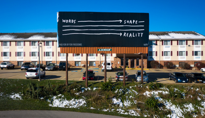 Photograph of a billboard, is black with white lines and lettering. At the top left it says ‘WORDS’ followed by a long line with an arrow pointing to ‘SHAPE’, three more lines are below, at the end the word 'REALITY'