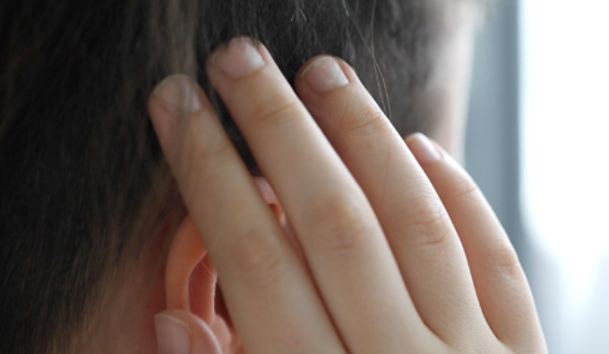 Close up of the side of a person's head. The hair is cropped very short, they are holding their hand uo to the head almost obscuring their ear.
