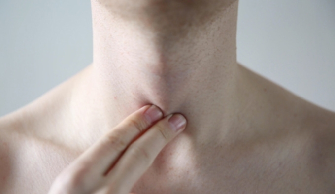 Close up of a person's throat. They are holding two fingers to their throat.
