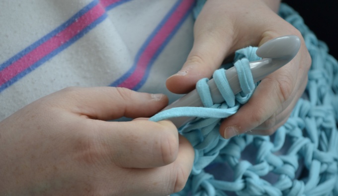 Two white hands crochet with crochet needle and thick turquoise blue cord.