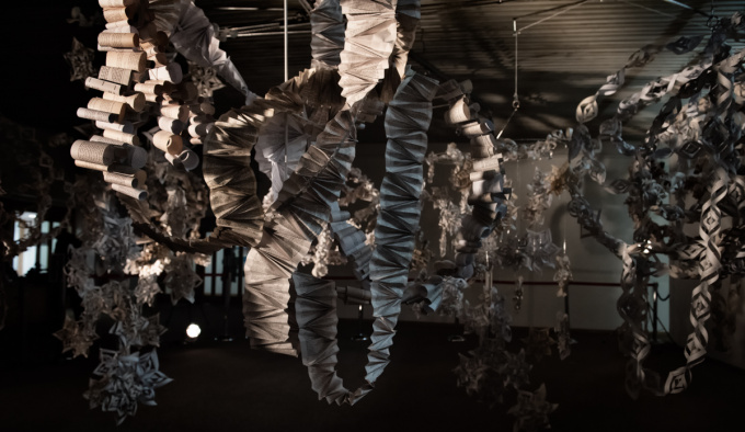 Paper streamers hang and loop from the ceiling, some are rolls of printed paper, or concertinaed fans, some take the form of snowflakes.