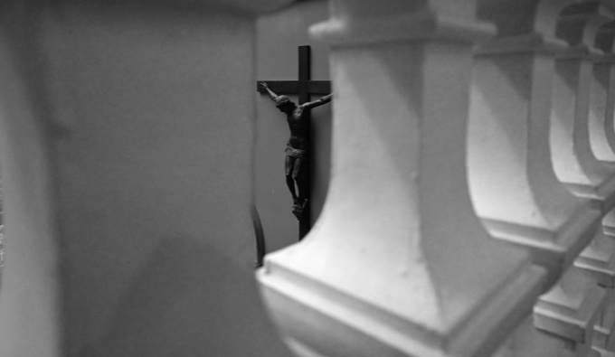 A black and white photo of a view through white stone pillars of a sculpture of Christ on the cross