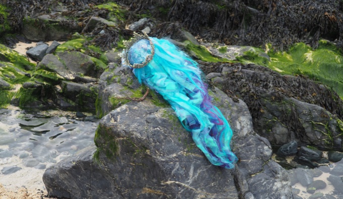 The bright blue and wig and crown of the artists costume is discarded on a rock on the beach. 