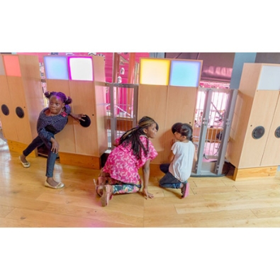 Children press their ear to the sound canvas, a set of wooden cabinets with a speaker and light panel.