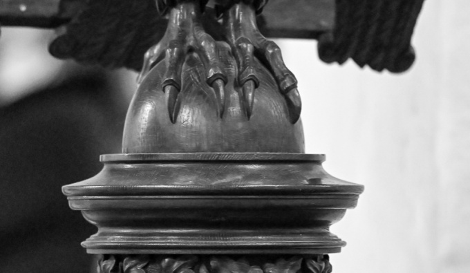 A black and white image of the caved feet of an eagle falling beneath a wooden lecturn.