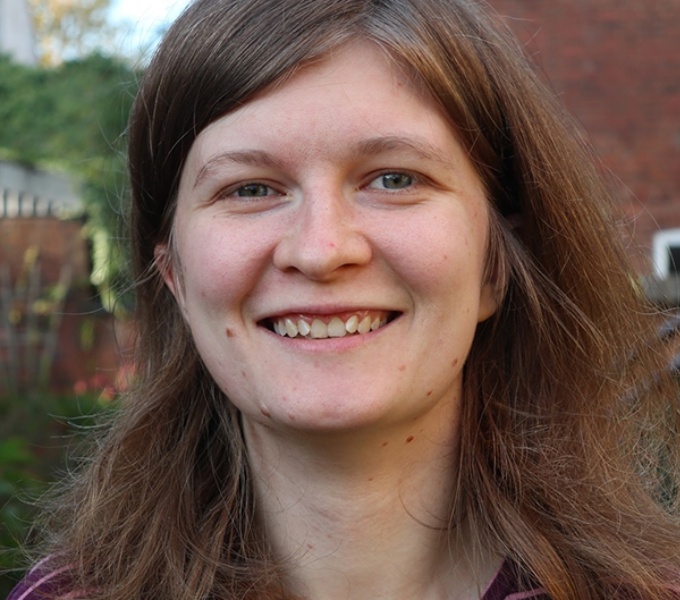 Jazz Moreton smiles at the camera . She has mid length, brown, red hair, green eyes and wears a purple stripey top.