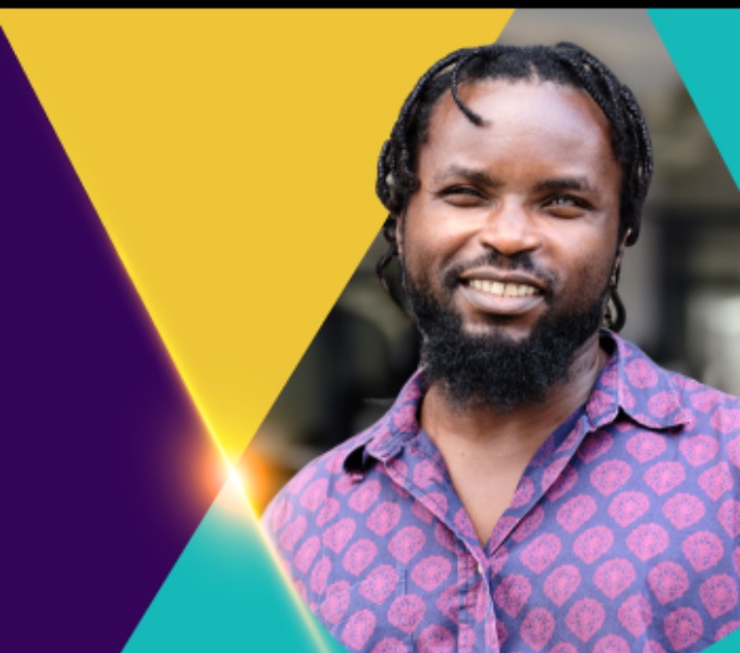 A background of purple, yellow and turquoise green triangles. In the foreground is a black man wearing a purple shirt with a pink pattern. He looks toward the camera and smiles. 