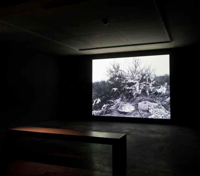 Juan's film Altered Landscapes is being projected onto a wall in the gallery space, in the foreground is a bench. 