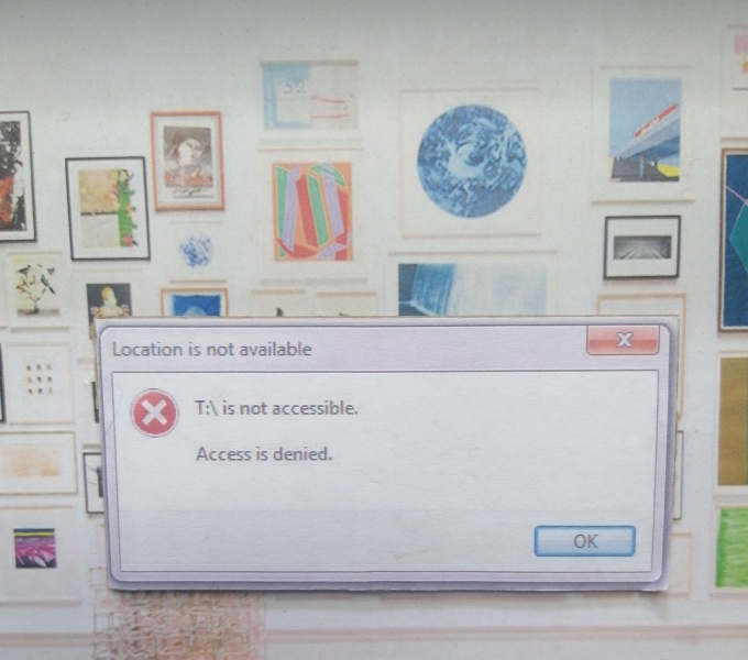 A computer screen with the warning pop up: Access Denied. In the background is the screensaver of a gallery space with various art works mounted onto a white wall.