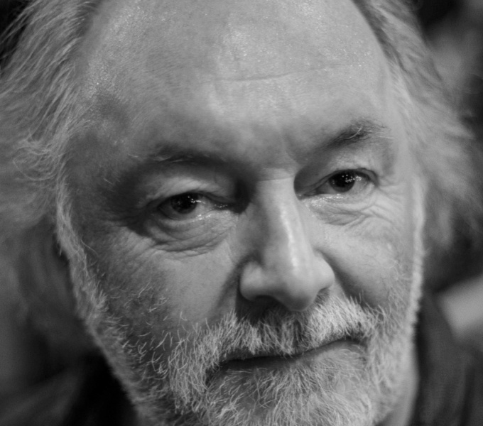 A black and white portrait photograph of Chris Tally Evans. He has thinning white hair and white stubbly beard.