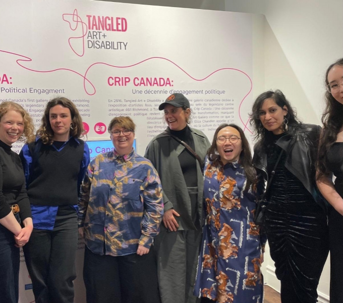 Members of the DASH and Tangled teams stand in a group in front of exhibition boards at the Crip Canada exhibition
