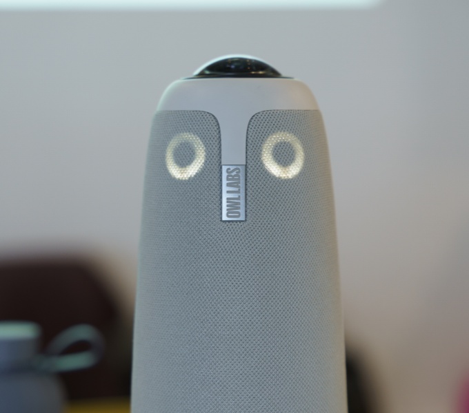 A close up picture of the 360 degree owl camera and microphone. It is owl shaped, with 2 circular lights like owl eyes showing that it is on.