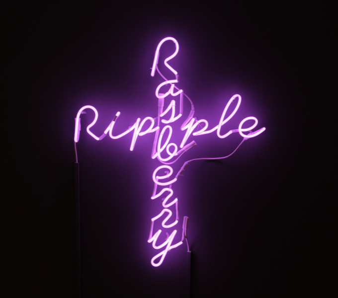 THe words Rasberry and Ripple in bright neon pink make the sign of a cross on a black background.