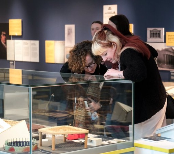 Two women peer into a glass cabinet of exhibits.