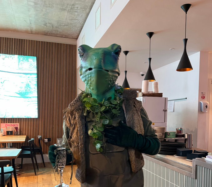 A man dressed as a frog stands in a cafe bar
