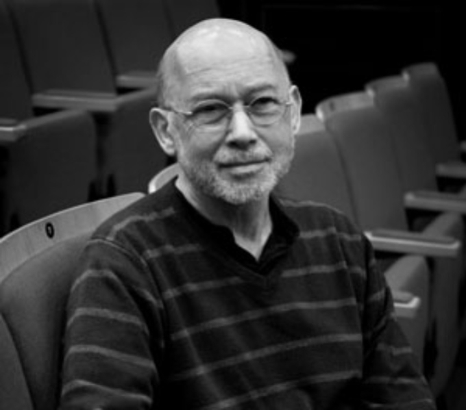 A black and white photographic portrait of Jonathan Hyams sat on theatre seating.