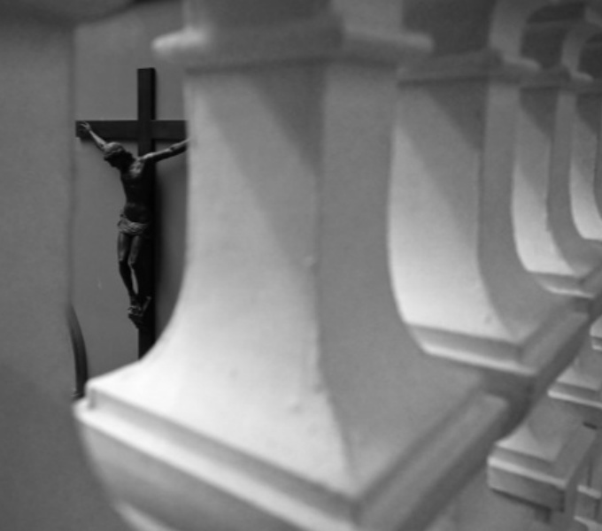 A black and white photo of a view through white stone pillars of a sculpture of Christ on the cross.