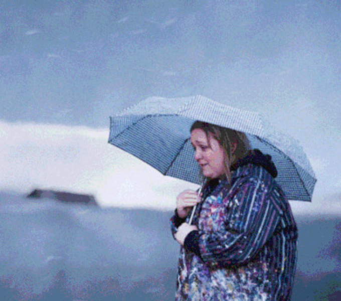 Artist Grace Currie cowers beneath an umbrella on a stormy day