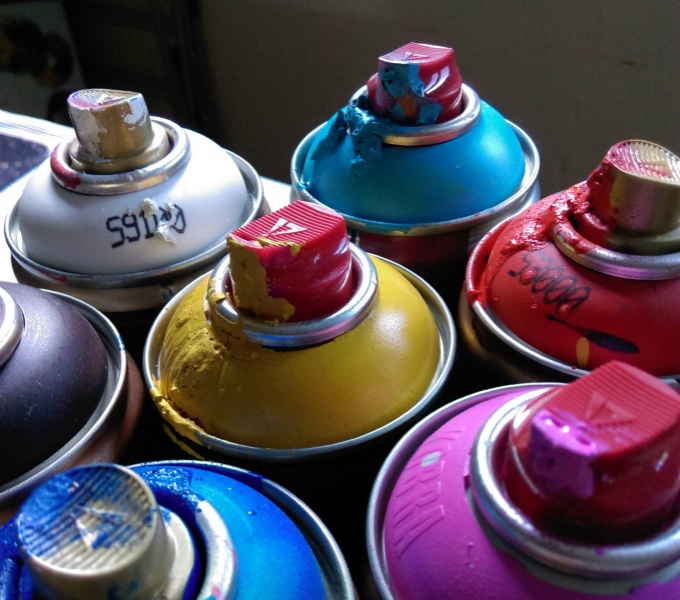 Assorted spray cans in blue, pink, yellow, red, white. Paint dribbles from the nozzles.