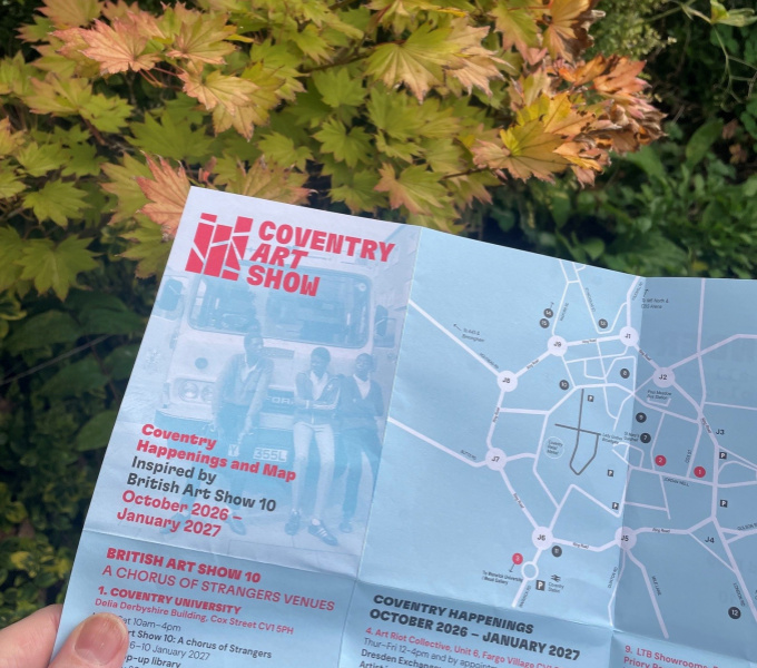 A hand holding  aprinted art show map on blue paper with an Autumnal coloured tree behind it.