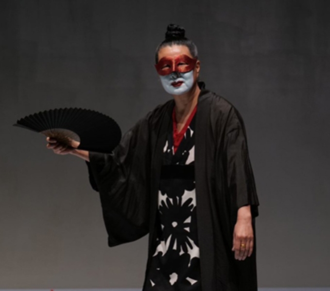 A photo of Wen Liao in traditional Chinese garments. She is wearing a mask over her eyes and holding a fan.