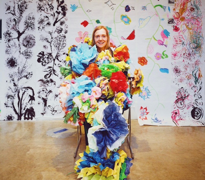 Jess Starns is covered in colourful paper against the backdrop of a wall covered in both colour and black and white drawings.