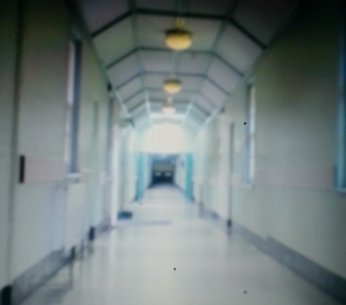 A white painted corridor lit with artificial lighting within an old building. The corridor disappears into the distance.