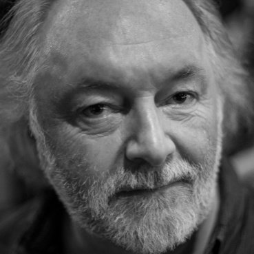 A black and white portrait photo of Chris.  He has a mid length white beard and dark shirt.