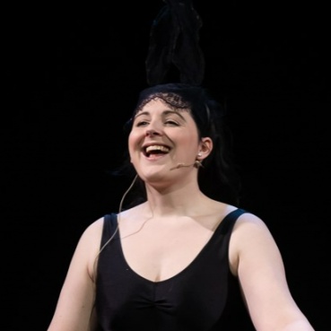 Porcelain stands against a black background and wears a black vest top. She is smiling as she speaks.