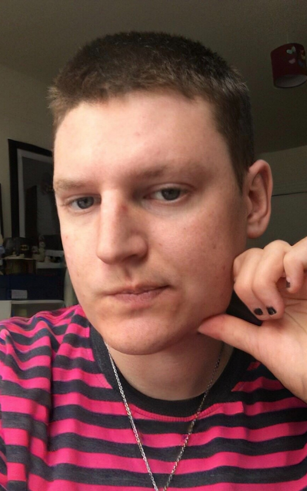 A close up portrait photo of Luca. They have short cropped hair and wears a red and black striped t-shirt and black painted nails and silver chain. 