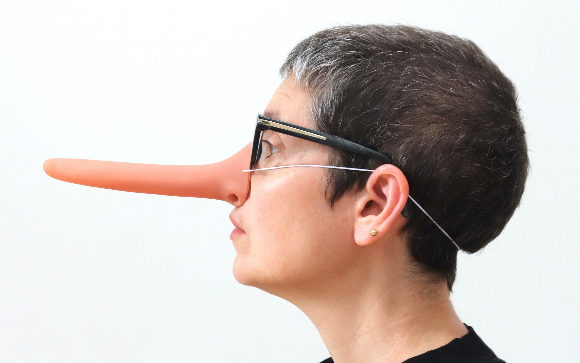 A side profile photographic portrait of Sonia with oversized elongated nose. She wears pink glasses and a black knitted hat.