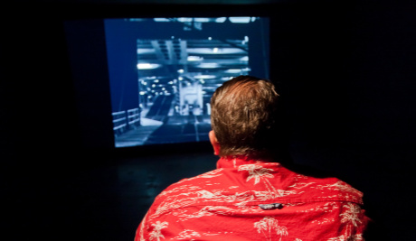 A photograph of the back of a man from behind looking at a blue screen. 