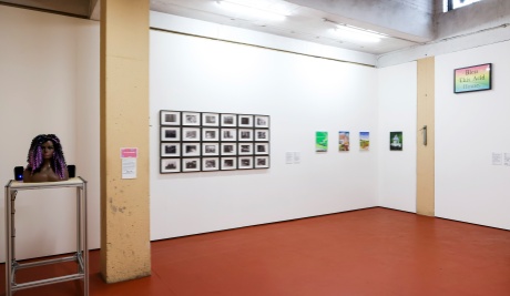 A large white gallery space with a brown, red floor. Exhibits are placed on the walls.
