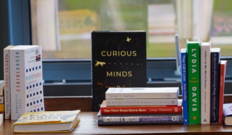 A selection of 13 books arranged in small piles and reflected in the window behind them.