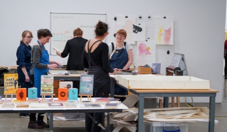 A group of people wearing aprons work in a studio space on print work