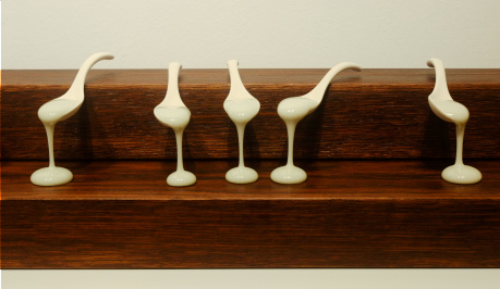 five white spoons resting on a piece of dark stained wood shelves , like steps, with white paint dripping onto the step below, creating a perfect round pool of paint underneath each spoon, a moment held in time, supended.