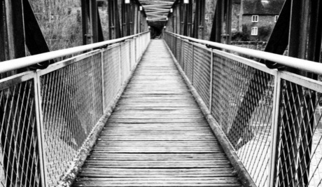 A black and white photograph of the centre of a bridge, looking down walkway into the distance.