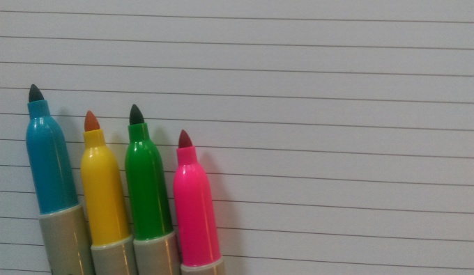 Blue, yellow, green and magenta pink pens on top of lined notebook 