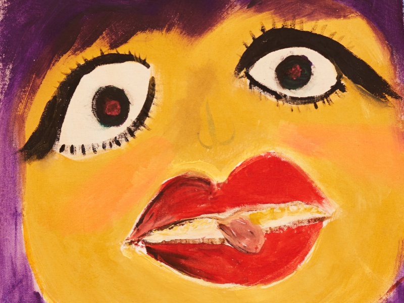 A hand painted close up of a face. The face is yellow in colour with large bright red lips and large eyes with apparent black eyeliner.