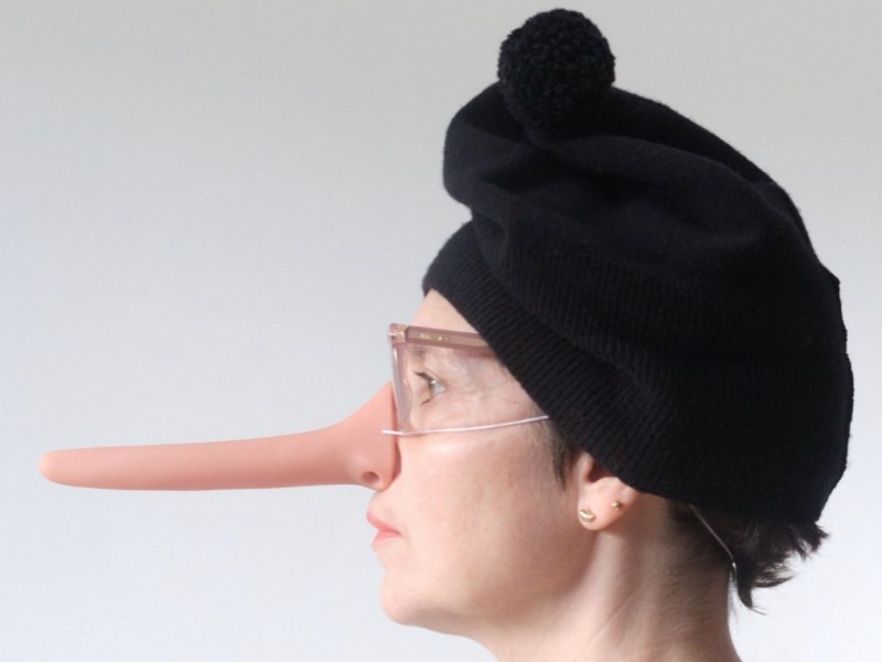A side profile photographic portrait of Sonia with oversized elongated nose. She wears pink glasses and a black knitted hat.