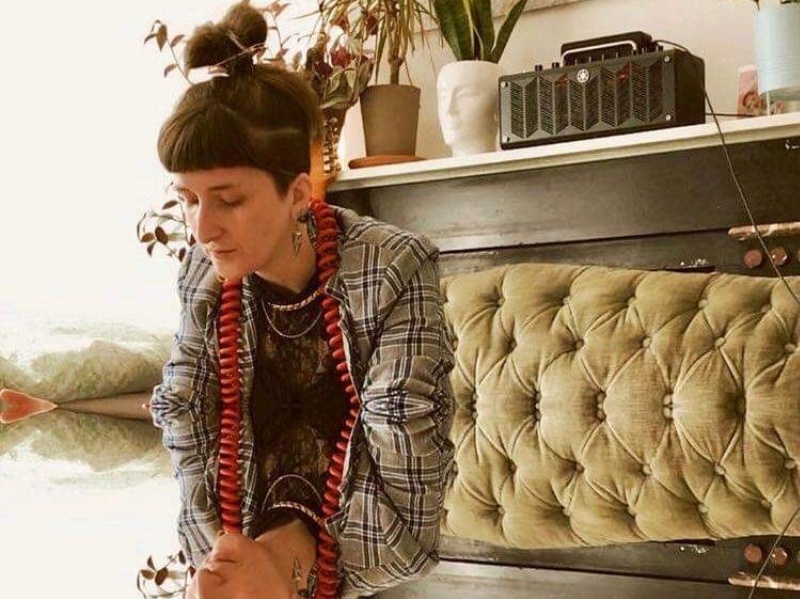 Stephanie wears a grey jacket, dangly earrings and hair tied back in a high bun. Steph and her surroundings are reflected as if in a mirror in the lower half of the image.