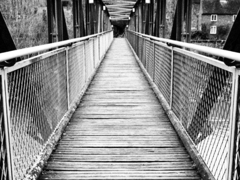 A black and white photograph of the centre of a bridge, looking down walkway into the distance.